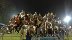 Equipo de futbol de uniforme blanco posando con trofeo sobre tarima