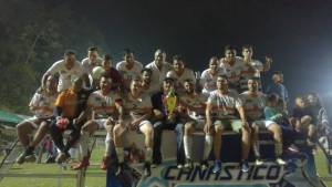 Equipo de futbol de uniforme blanco posando con trofeo sobre tarima